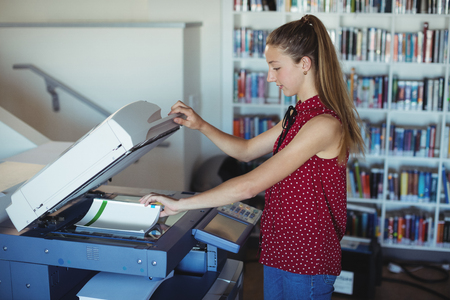 Attentive schoolgirl using Xerox photocopier in library at school