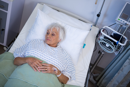 Thoughtful senior patient lying on bed in hospitalの写真素材