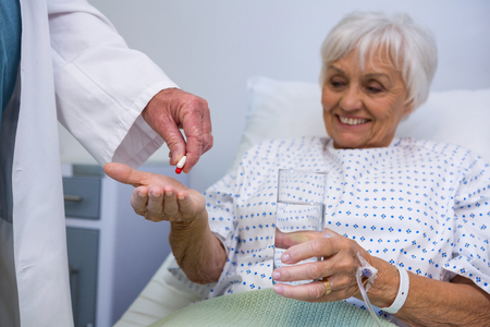 Doctor giving medicine pill to senior patient in hospitalの写真素材
