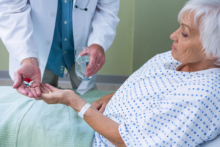 Doctor giving medicine pill to senior patient in hospitalの写真素材