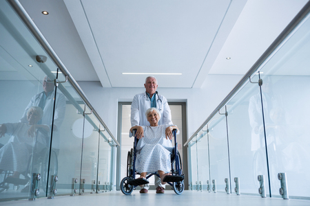 Doctor holding senior patient on wheelchair in passageway at hospitalの写真素材