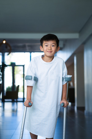Boy patient walking with crutches in corridor at hospitalの写真素材