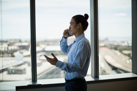 Business executive talking on mobile phone in corridor at officeの写真素材