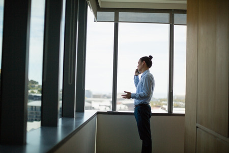 Business executive talking on mobile phone in corridor at officeの写真素材