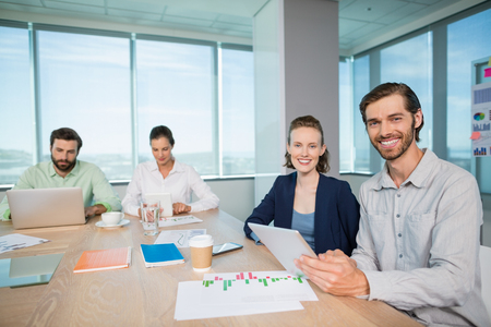 Portrait of smiling business executives sitting together in conference room with digital tablet at officeの写真素材
