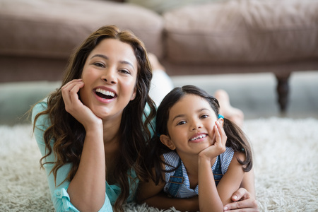 Portrait of happy mother and daughter lying on rug at homeの写真素材