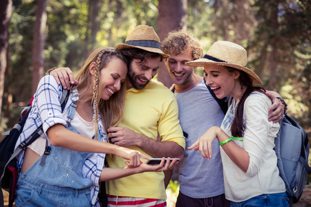 Woman showing mobile phone to friends in forest on a sunny day