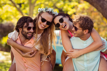 Men giving piggyback rides to women in park on a sunny dayの写真素材