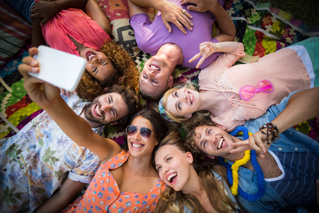Group of friends lying in a circle and taking selfie on a sunny dayの写真素材