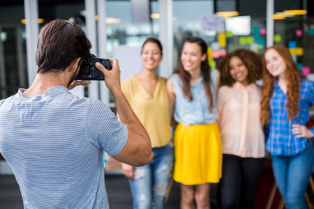 Man photographing his female colleagues with camera in officeの写真素材