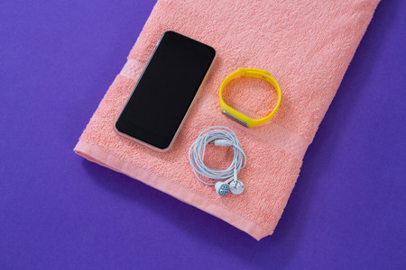 Towel with mobile phone, headphones and fitness band on purple backgroundの写真素材