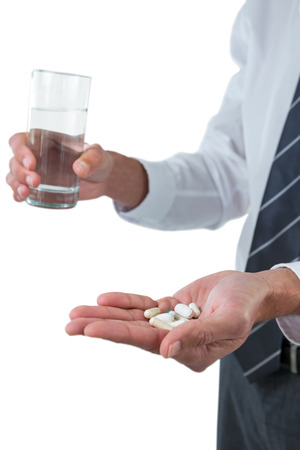 Businessman holding glass of water and medicines against white backgroundの写真素材