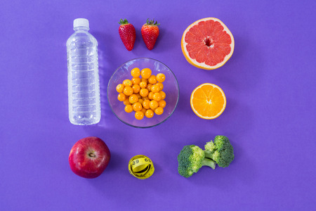 Water bottle, measuring tape, various fruits, vegetable and diet breakfast on purple background