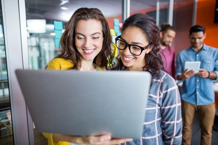 Two smiling female executives using laptop in officeの写真素材