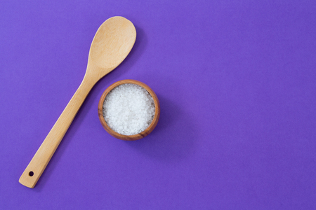 Salt in wooden bowl and scoop on purple backgroundの写真素材