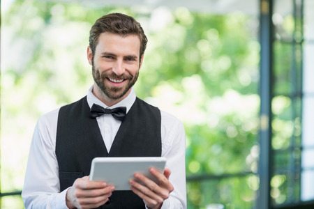 Portrait of male waiter holding digital tablet in restaurantの写真素材