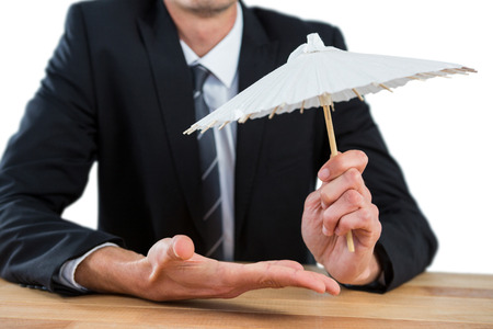 Businessman holding an paper umbrella against white backgroundの写真素材