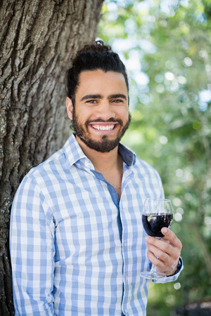 Portrait of man holding a glass of wine in the park on a sunny dayの写真素材