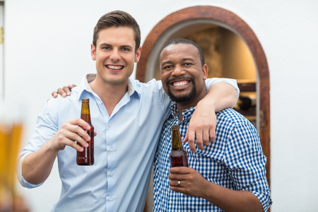 Friends hugging each other while holding beer bottles in the restaurantの写真素材