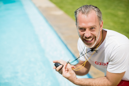 Portrait of swim coach holding stopwatch near poolside on a sunny dayの写真素材