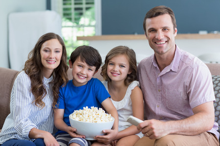 Portrait of smiling family watching tv and eating popcorn in living room at home
