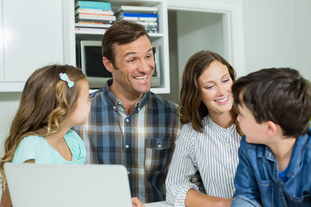Smiling family interacting with each other while using laptop in living room at homeの写真素材