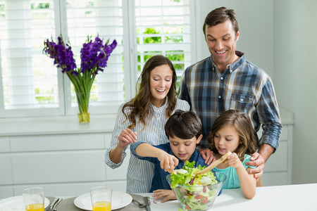 Smiling family preparing bowl of salad in kitchen at homeの写真素材