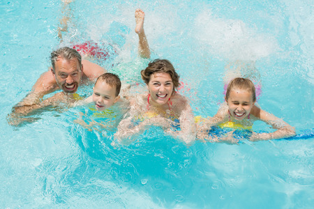 Portrait of happy parents and kids having fun in pool on a sunny dayの写真素材