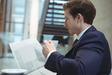 Businessman reading newspaper while having coffee at officeの写真素材