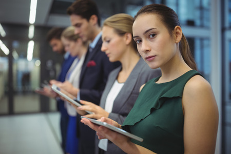 Business executives using electronic devices in corridor at office