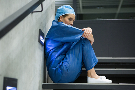 Thoughtful female surgeon sitting on staircase in hospitalの写真素材