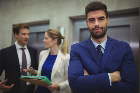 Portrait of handsome businessman standing with arms crossed in officeの写真素材