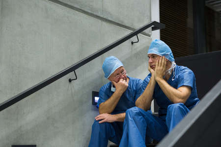 Worried male surgeons sitting on staircase in hospitalの写真素材