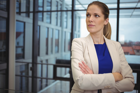 Thoughtful businesswoman standing with arms crossed in corridor in corridorの写真素材