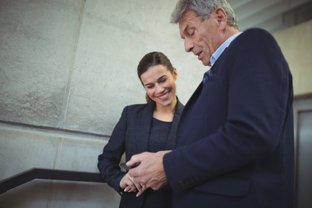 Businesspeople discussing over electronic device in corridor at officeの写真素材