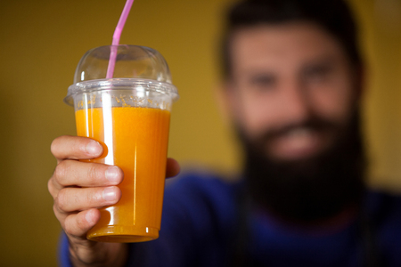 Male staff holding orange juice glass at organic section of supermarketの写真素材