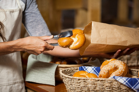 Mid-section of staff packing bread in paper bag at bakery shop