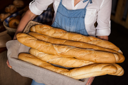 Mid-section of female staff holding basket of baguettes in bakery section of supermarketの写真素材