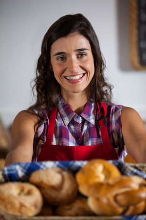 Portrait of female staff holding basket of sweet foods in supermarketの写真素材