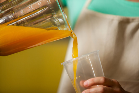 Female staff pouring juice into glass at counter in health grocery shopの写真素材