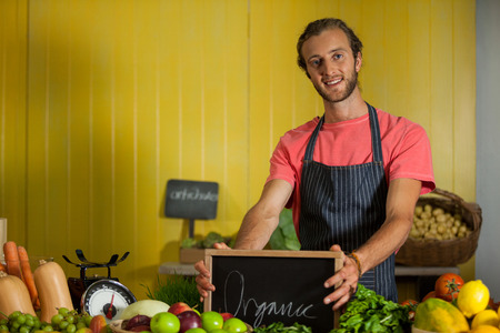 Portrait of male staff holding slate board in organic section of supermarketの写真素材