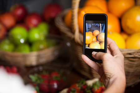 Female costumer taking picture of oranges on mobile phone in organic section of supermarketの写真素材