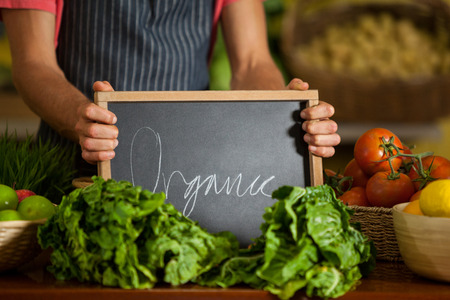 Mid section male staff holding slate board in organic section of supermarketの写真素材