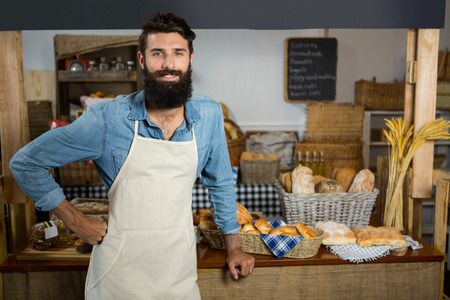Portrait of smiling male staff standing with hands on hip at counter in bakery shop