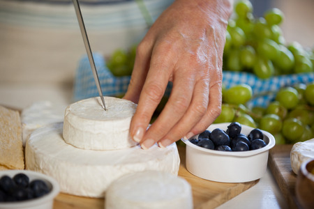 Mid section of female staff slicing cheese at counter of supermarketの写真素材