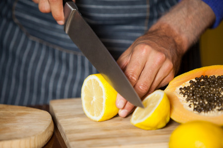 Mid-section of male staff cutting lemon in organic section of supermarketの写真素材
