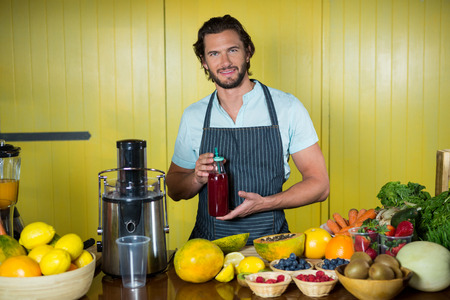 Portrait of smiling male staff holding juice bottle at counter in health grocery shopの写真素材