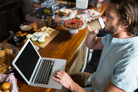 Man having coffee while using laptop at counter in coffee shopの写真素材