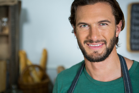 Portrait of smiling male staff standing with arms crossed in bakery shopの写真素材