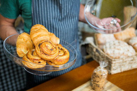 Staff holding tray of croissant at counter in bakery shopの写真素材